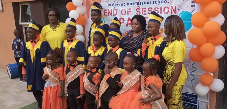 Pupils in graduation gowns and orange outfits with teachers at an end-of-session party
