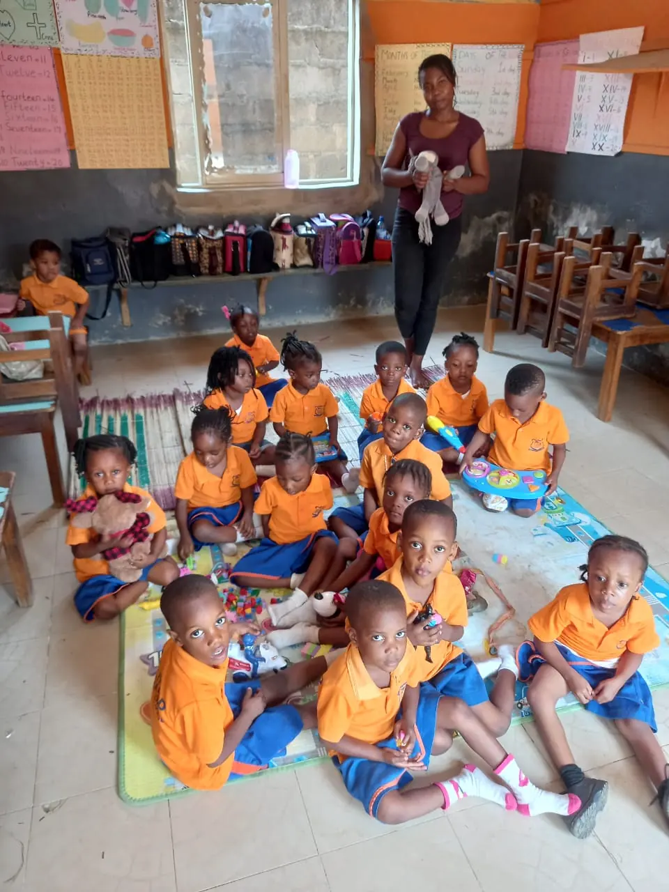 Nursery pupils in orange uniforms sitting on a play mat with their teacher