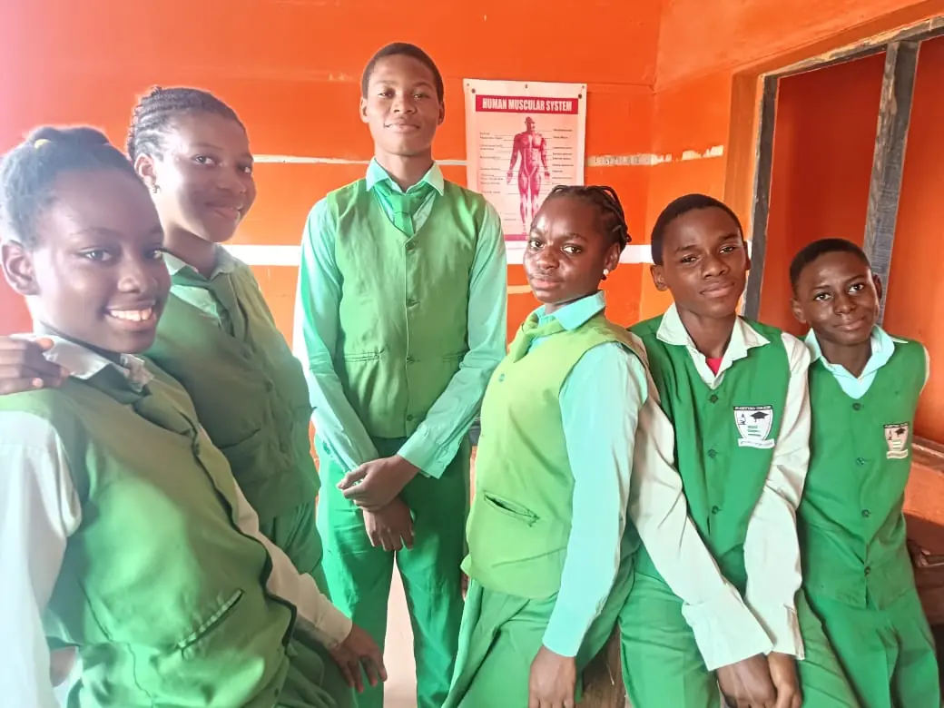 Secondary students in green uniforms smiling in a classroom